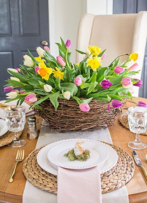 a large nest with bright tulips and daffodils, moss with bunnies and wicker chargers for a spring table