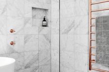 a marble tile bathroom with a dark floor, a tub, a shower and copper hardware for a chic and bold look