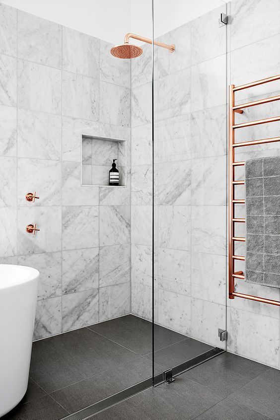 a marble tile bathroom with a dark floor, a tub, a shower and copper hardware for a chic and bold look