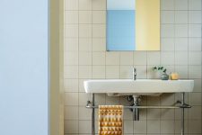 a modern bathroom clad with tan tiles and with matching but colorful tiles on the floor, with a free-standing sink and a rectangular mirror