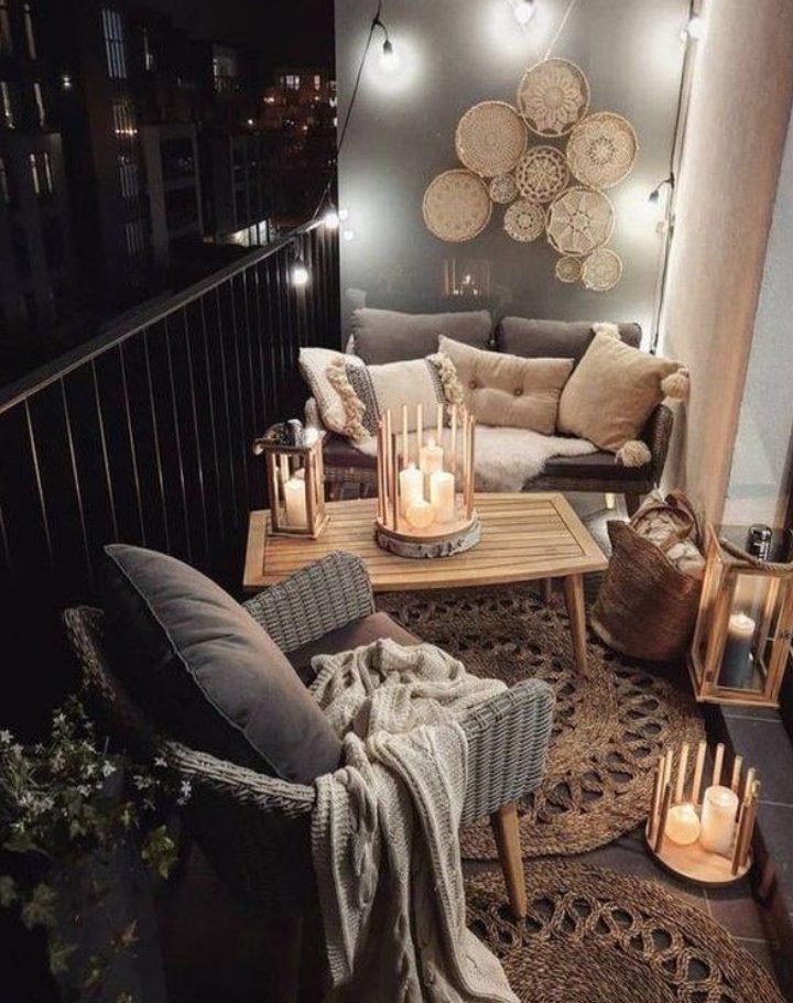 a modern meets boho balcony with a grey sofa and a wicker chair, a wooden table, jute rugs, candle lanterns and an arrangement of decorative baskets