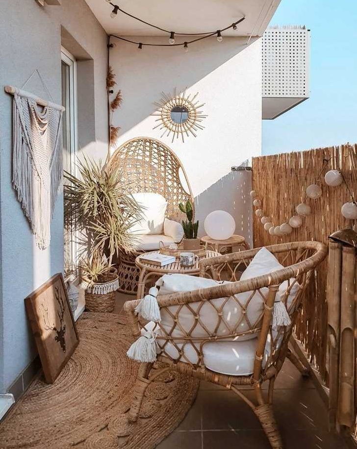 a neutral boho balcony with rattan boho furniture, a jute rug, a macrame hanging, a sunburst mirror, some potted plants and cacti is very welcoming