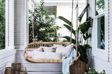 a neutral tropical boho porch with a rattan hanging seat, potted greenery, candle lanterns and jute rugs