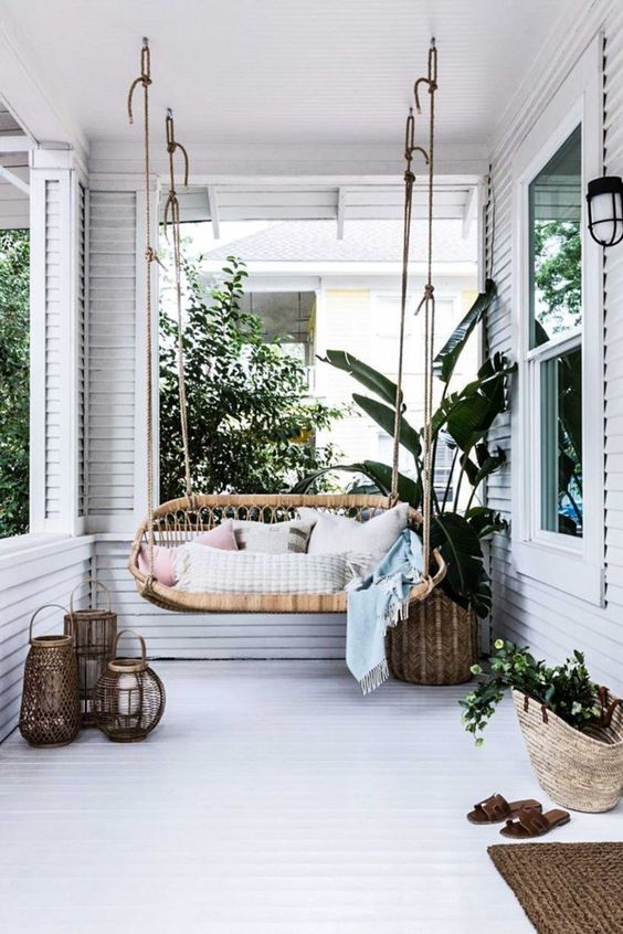 a neutral tropical boho porch with a rattan hanging seat, potted greenery, candle lanterns and jute rugs