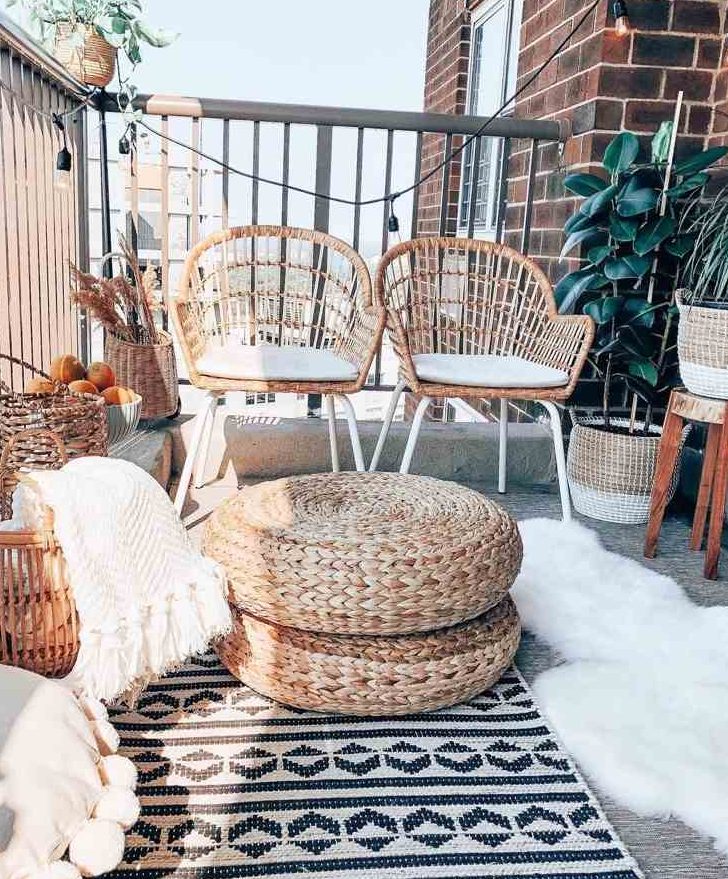 a pretty boho balcony with black and white rugs, faux fur and white blankets, wicker chairs, candle lanterns and jute poufs, potted plants is amazing for spending time here