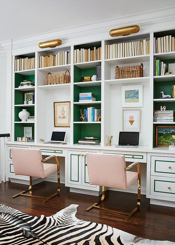 a refined home office with built-in bookshelves with green backing and pink metallic chairs and a faux zebra rug