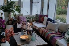 a screened boho porch with a sectional styled with bright printed textiles, a low wooden table with candles and lights and blooms