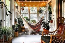 a screened porch with a macrame hammock, potted plants, lights and rattan furniture plus boho rugs