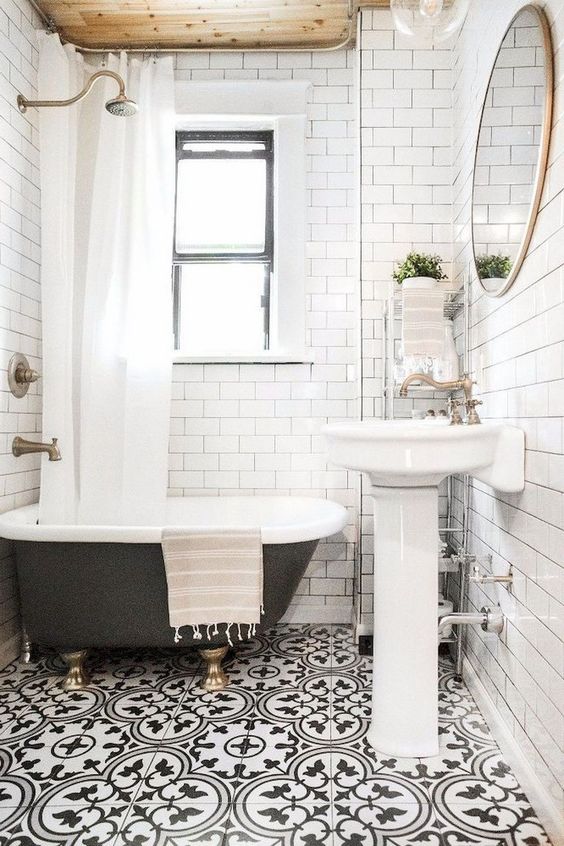 a small and bright bathroom with a mosaic floor, a wooden ceiling, a black clawfoot tub and a free-standing sink