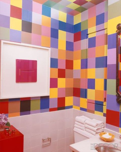 a small and colorful powder room with super bright tiles all over it, a red cabinet and a free-standing sink plus a bold artwork