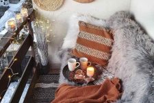 a small boho balcony with a sofa with faux fur, some pillows and blankets, a printed rug and some woden placemats and lights is cool