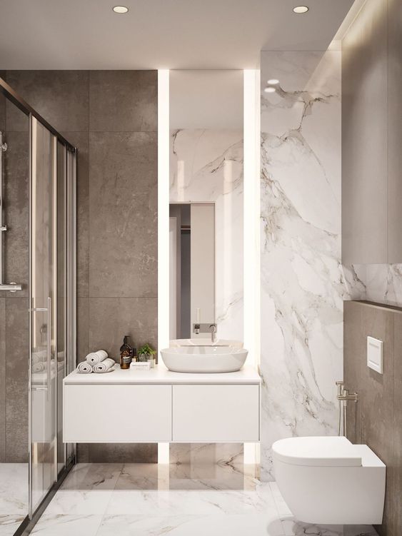 a small minimalist bathroom with marble tiles, a shower space, a floating vanity and a tall mirror with lights