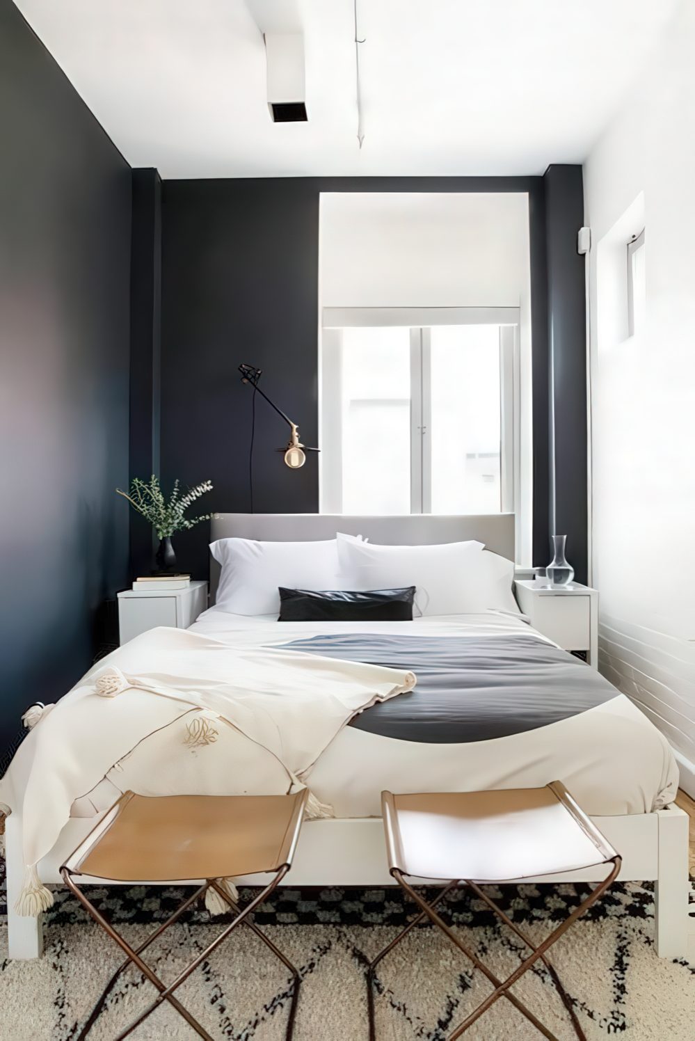 a small modern bedroom with black and white walls, a grey bed, leather stools and lamps and bulbs