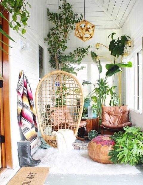 a small screened boho porch with a rattan hanging chair, leather loungers, potted greenery and lots of potted greenery
