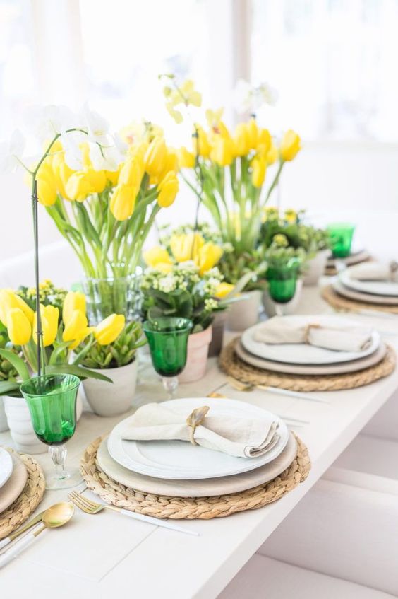 a spring tablescape with bright yellow tulips, fresh greenery and green glasses looks bold, fresh and very spring-like