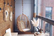 a stylish and laconic boho balcony with a jute rug, a cork bench, a rattan hanging chair, some pampas grass, rattan stools and a basket and paper pendant lamps