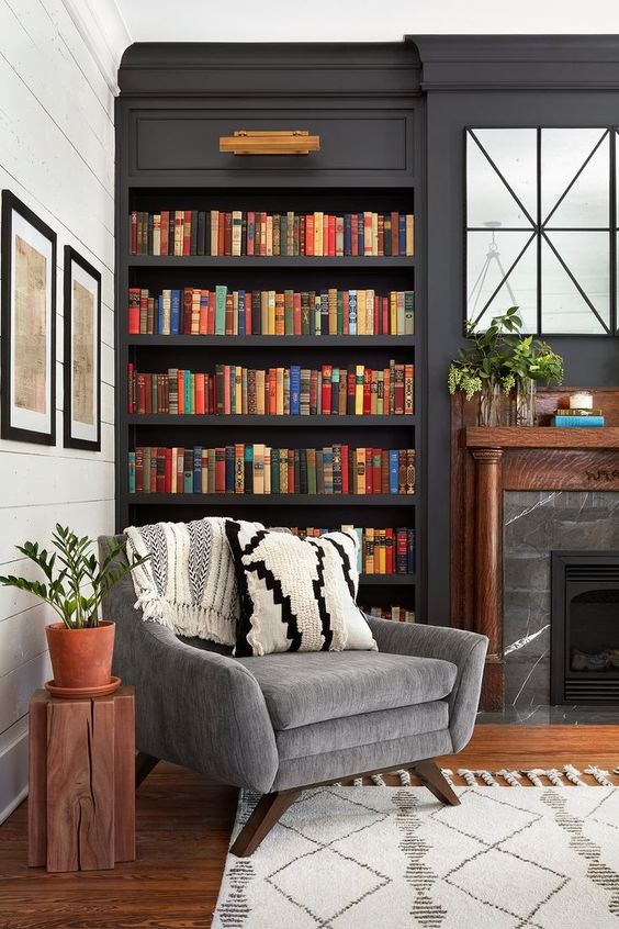 a stylish moody space with dark built-in bookshelves, a marble fireplace and a grey chair for much comfort