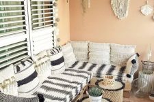 a terracotta-colored balcony with a corner pallet sofa with black and white upholstery, coffee tables and cork tables, macrame and hanging greenery