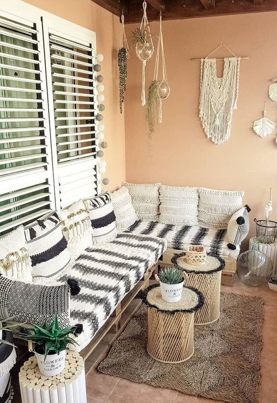 a terracotta colored balcony with a corner pallet sofa with black and white upholstery, coffee tables and cork tables, macrame and hanging greenery