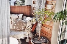 a tiny boho balcony with a bench with boho pillows and blankets, potted plants and greenery, a dream catcher, a jute rug and a wood slice table