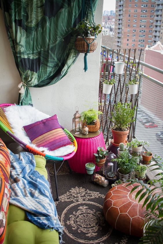 a tiny colorful boho balcony with a black rug, a neon green bench, a multicolor chair, lots of potted plants and cacti, some pillows