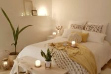 a tiny neutral bedroom with catchy bedding and a chunky knit blanket, a wooden bench, potted greenery and candles