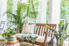 a tropical boho porch with wooden furniture, jute rugs, lots of potted greenery and candle lanterns