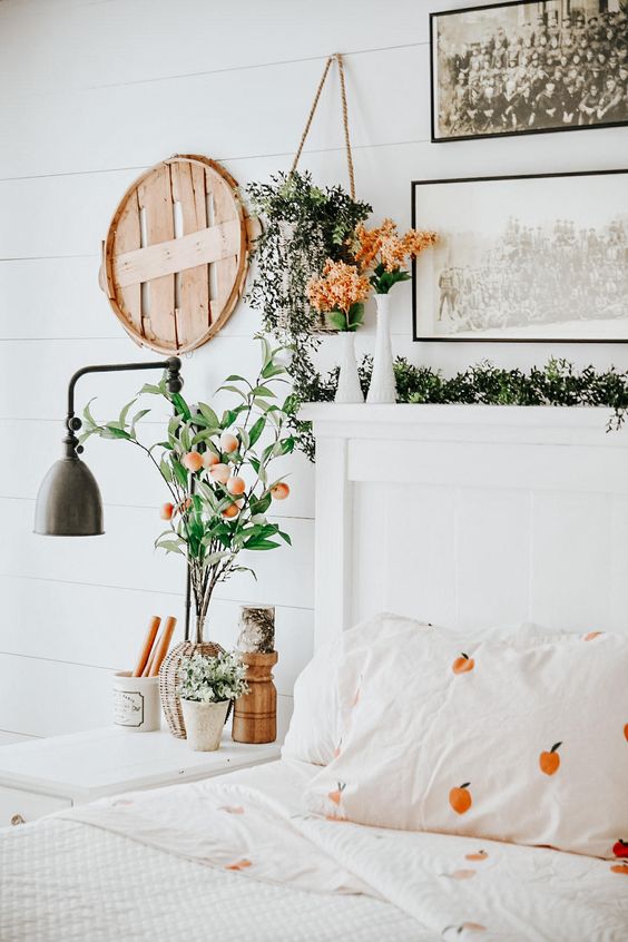 a welcoming spring bedroom in neutrals, with pretty artworks, greenery and blooms, a wall sconce, printed bedding