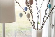 a white vase with willow and colorful and pastel eggs hanging on them will be a nice Easter decoration