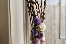 an Easter centerpiece of a tall clear vase with colorful eggs and willow is a chic idea