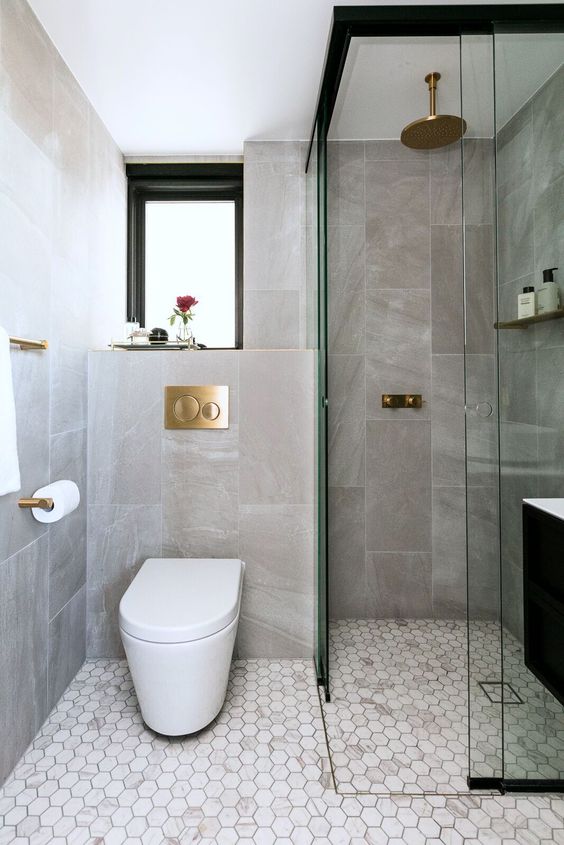 an elegant contemporary bathroom with stone and marble tiles, a window, a shower space and gilded touches