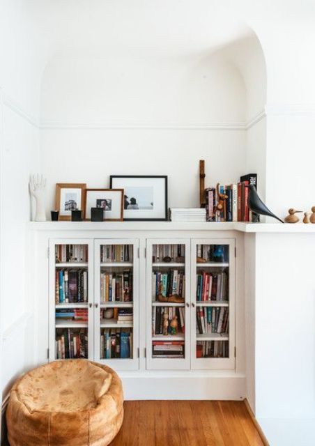 built-in bookshelf units with glass doors and a small pouf for a cozy reading nook