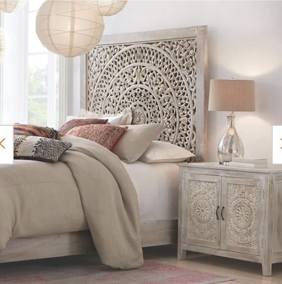 a Moroccan-inspired neutral bedroom with a whitewashed carved wooden headboard and a matching cabinet, neutral bedding, paper pendant lamps and a table lammp