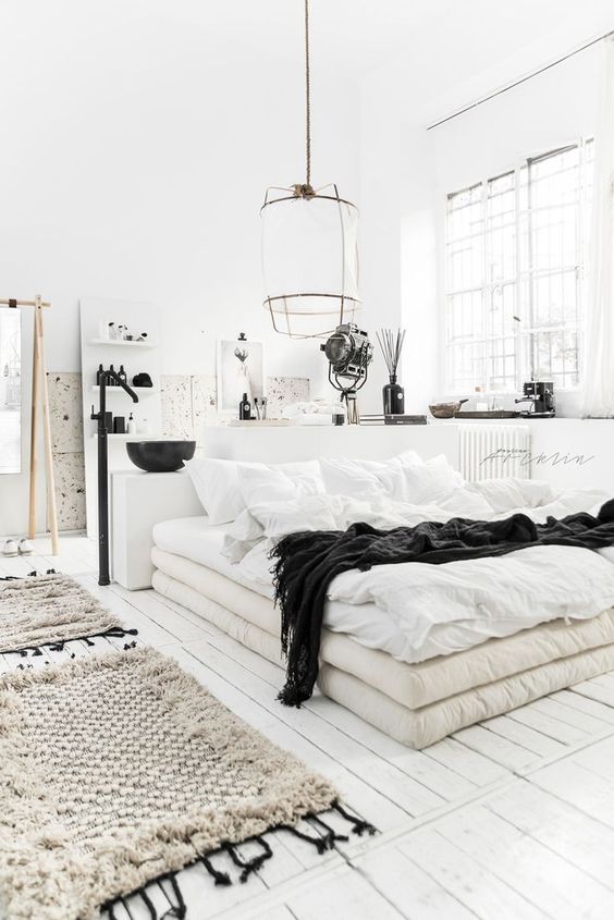 a Nordic bedroom with a bathroom here, with white walls and a whitewashed floor, simple furniture and black touches for drama