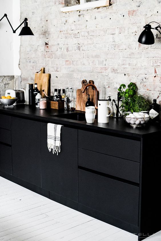a Nordic kitchen with a whitewashed brick wall, black sleek cabinetry, black sconces and some herbs in pots is a very stylish space