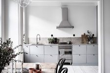 a Scandinavian space with white walls and whitewashed floors, grey cabinets, a wooden table and black chairs