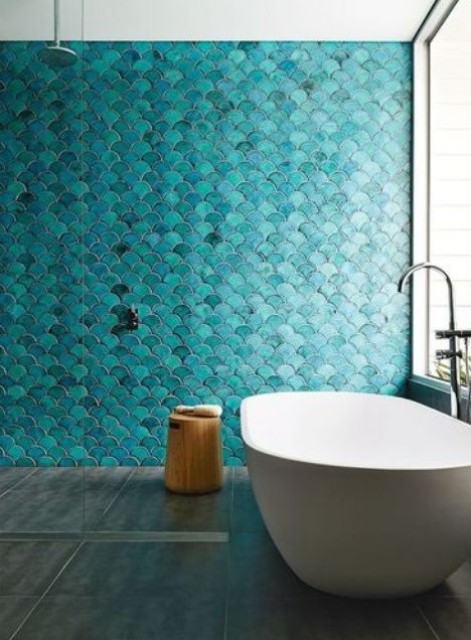 a beautiful contemporary bathroom with a turquoise fish scale tile wall, a white tub and a wooden stool is lovely