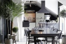 a bold kitchen and dining room, wiht white wood and plaster walls, a whitewashed floor and black furniture and pendant lamps