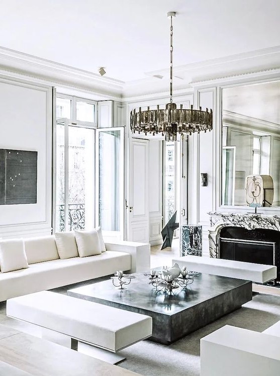 a breathtaking French chic living room with a marble fireplace, a stone slab table, white and creamy seating furniture and a statement chandelier