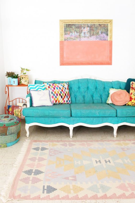 a bright boho space with a vintage turquoise sofa, colorful pillows and a rug, an orange side table with plants and a bold artwork