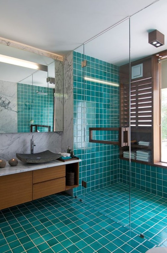 a bright modern bathroom with turquoise tiles, marble walls, a wooden vnaity, a stone sink and a statement mirror