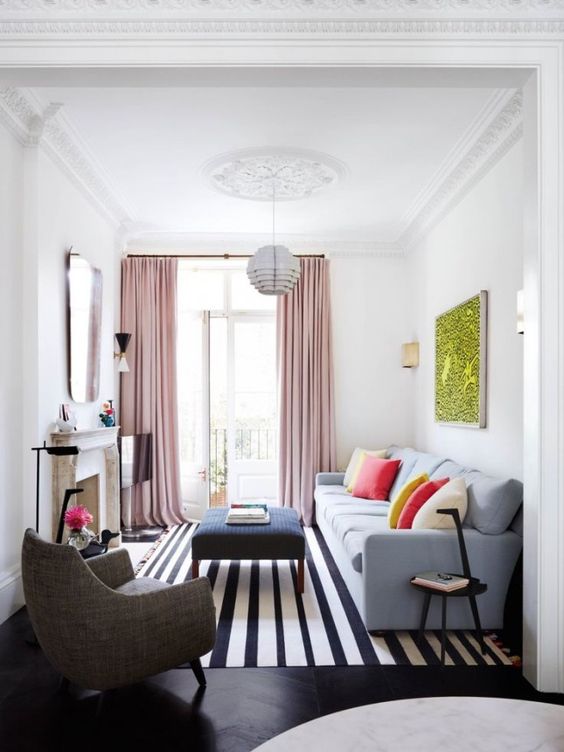 a bright small living room with a molded ceiling, pink curtains, bright pillows, a striped rug and a non-working fireplace for coziness