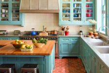 a bright turquoise kitchen with shaker style cabinets, a large metal hood, a large kitchen island with butcherblock countertops and terracotta hexagon tiles on the floor