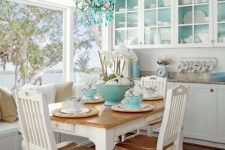 a charming breakfast nook with white vintage furniture, a table with a stained tabletop, turquoise backing in the cabinets, a turquoise chandelier and bowls