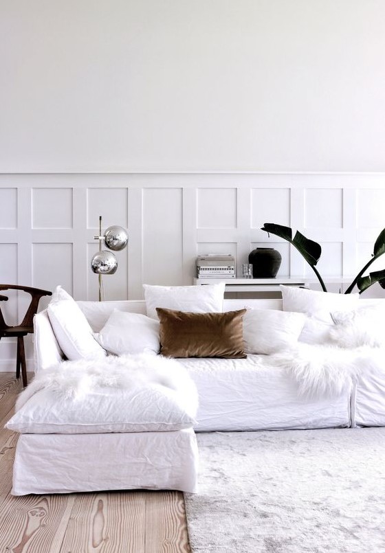 a chic Scandinavian living room with paneling, a white sectional, white pillows, a stylish floor lamp and some plants