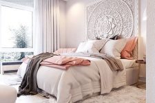 a chic bedroom with a whitewashed carved headboard, a bed with neutral bedding, a fluffy rug, white chairs and a large window