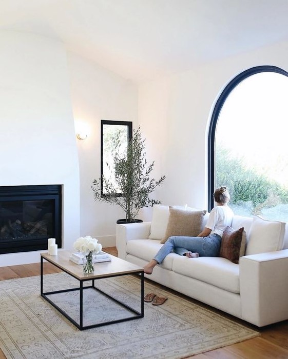a chic neutral living room with an arched window, a built-in fireplace, a white sofa and a coffee table and a potted mini tree