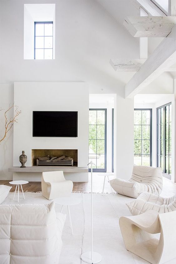 a chic white living room with lots of natural light, a faux fireplace, white furniture, side tables and a floor lamp