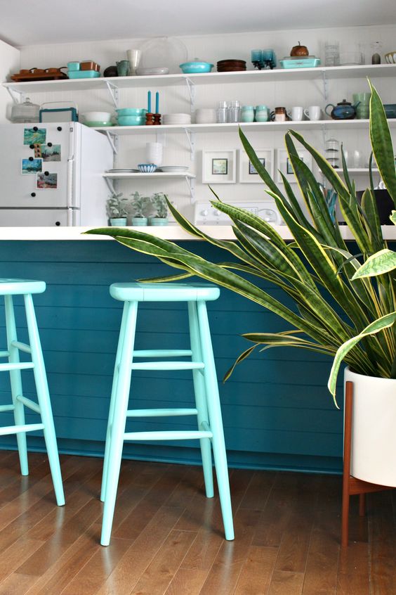 a coastal kitchen with white open shelves, a navy kitchen island, turquoise stools and various bowls and plates looks cool and fun