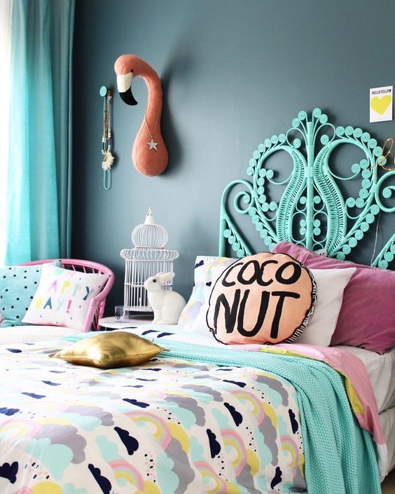 a colorful bedroom with a black accent wall, a hot pink chair, a turquoise bed, bright printed bedding, a flamingo head on the wall